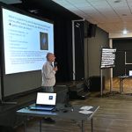 Intervenant faisant une présentation avec un écran derrière lui