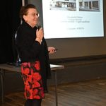 Intervenante faisant une présentation avec un écran derrière elle